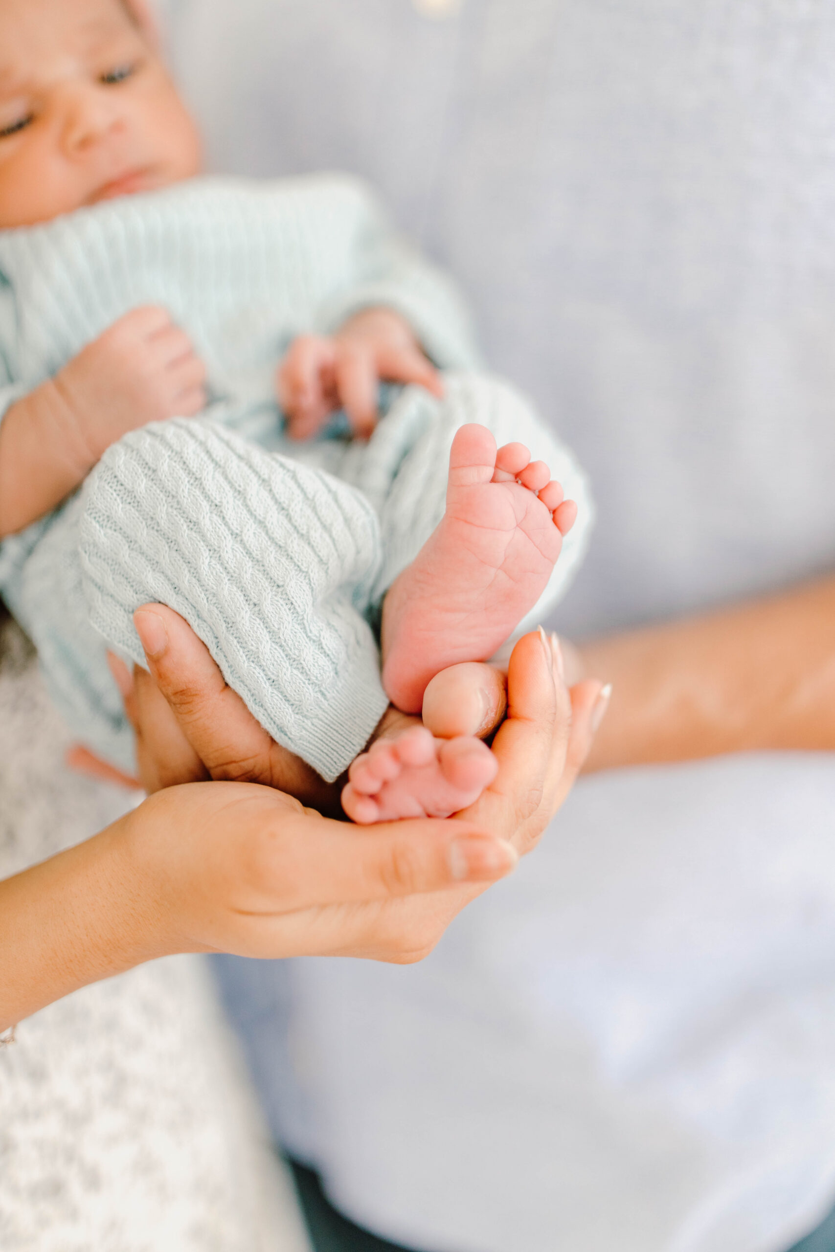 A parent’s hands cradling a newborn’s tiny feet, baby wearing a soft mint knit outfit